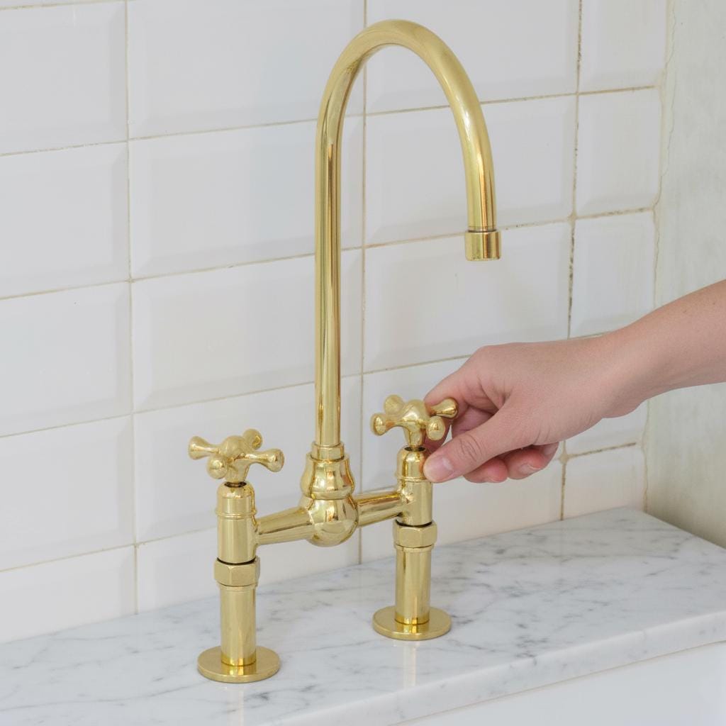 Gold kitchen faucet with a hand turning the handle against a tiled wall background
