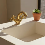 Gold faucet on a white sink with a potted plant in the background