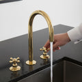 Gold kitchen faucet with a hand turning the handle on a black countertop.
