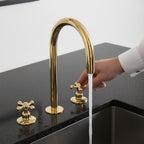 Gold kitchen faucet with a hand turning the handle on a black countertop.