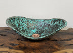 Decorative glass bowl with a green and brown speckled pattern on a wooden surface.