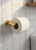 Gold toilet paper holder with a roll of toilet paper on a tiled bathroom wall.