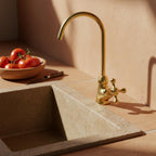 Gold faucet over a stone sink with tomatoes in the background