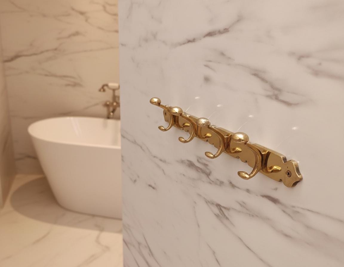 Gold decorative wall hook on a marble bathroom wall with a bathtub in the background.