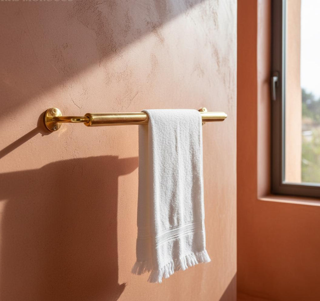 Gold towel rack with a white towel on a peach-colored wall.