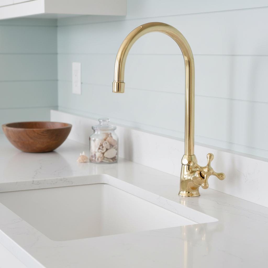 Gold kitchen faucet over a white sink with a light blue tiled wall in the background.