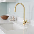 Gold kitchen faucet over a white sink with a light blue tiled wall in the background.