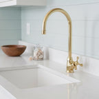 Gold kitchen faucet over a white sink with a light blue tiled wall in the background.