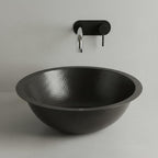 Black hammered sink with a wall-mounted faucet on a light gray background